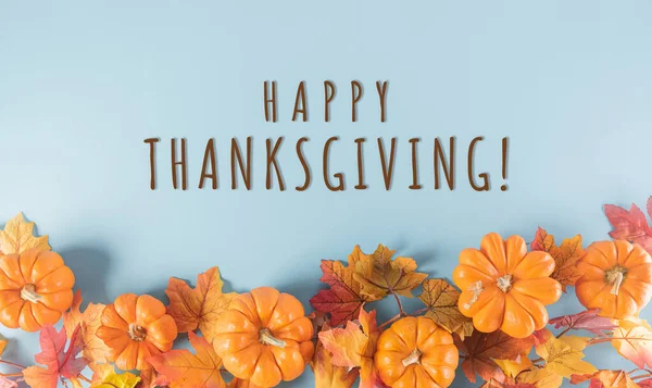 Thanksgiving background decoration from dry leaves and pumpkin on  pastel blue background. Flat lay, top view with Thanksgiving text.