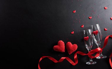 Sevgililer Günü ve aşk konsepti şampanya bardakları ve siyah tahta arka planda kırmızı kalplerden yapılmıştır. Kopyalama alanı olan üst görünüm, düz yatay.