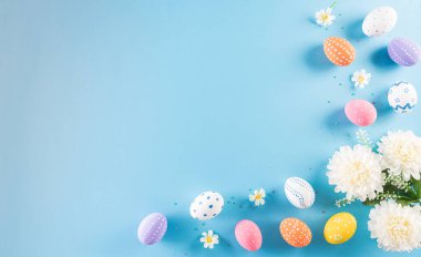 Mutlu Paskalyalar! Pastel mavi arka planda çiçekli bir sürü Paskalya yumurtası. Paskalya Günü için hediyeler ve selamlar zamanı kutluyor. Düz yatış, üst görünüm.