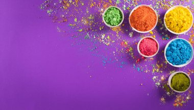 Mutlu Holi Festivali dekorasyonu. Mor arkaplandaki renkli holi tozunun üst görüntüsü. Metin için kopya alanı da var..