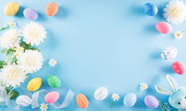 Mutlu Paskalyalar! Pastel mavi arka planda çiçekli bir sürü Paskalya yumurtası. Paskalya Günü için hediyeler ve selamlar zamanı kutluyor. Düz yatış, üst görünüm.