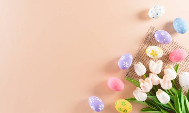 Mutlu Paskalyalar! Renkli paskalya yumurtaları ve pastel arka planda çiçekler. Paskalya Günü için hediyeler ve selamlar zamanı kutluyor. Düz yatış, üst görünüm.