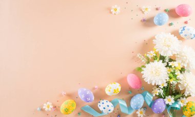Mutlu Paskalyalar! Renkli paskalya yumurtaları ve pastel arka planda çiçekler. Paskalya Günü için hediyeler ve selamlar zamanı kutluyor. Düz yatış, üst görünüm.