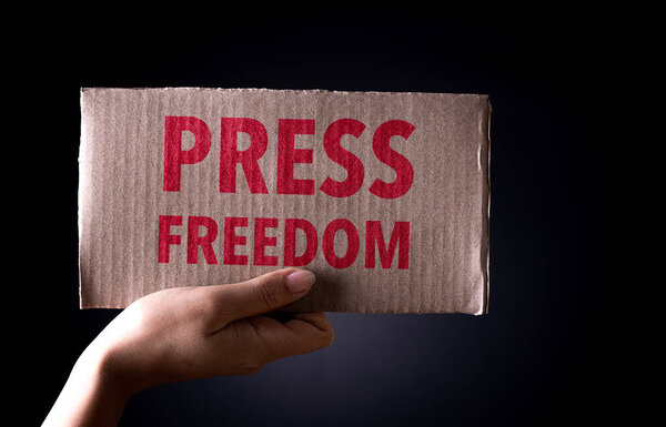 World press freedom day concept. Hand  holding cardboard paper with the text on dark background, conceptual image, symbol of press or speech freedom.