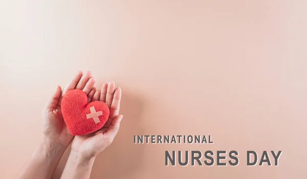 Hand holding red heart on pastel background. International nurse day and medical concept.