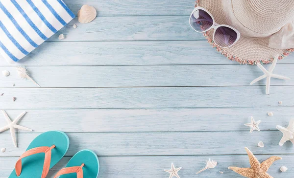 Yaz tatili, seyahat ve tatil konsepti. Güneş gözlüğü, denizyıldızı, plaj şapkası, terlik ve deniz kabuğu pastel mavi ahşap arka planda..