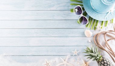 Yaz tatili, seyahat ve tatil konsepti. Güneş gözlüklü plaj şapkası, denizyıldızı, halat, ananas ve deniz kabuğu pastel mavi ahşap arka planda..