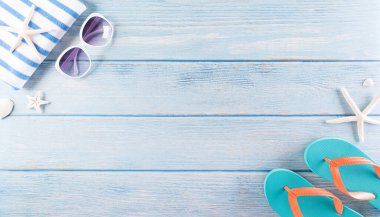 Yaz tatili, seyahat ve tatil konsepti. Güneş gözlüğü, denizyıldızı, terlik ve deniz kabuğu pastel mavi ahşap arka planda.