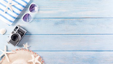 Yaz tatili, seyahat ve tatil konsepti. Güneş gözlüğü, denizyıldızı, retro kamera ve pastel mavi ahşap arka planda deniz kabuğu..