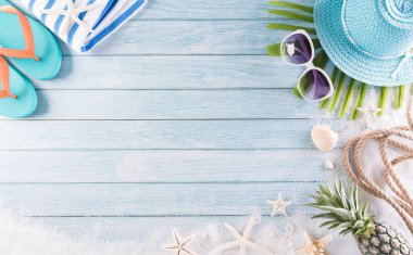 Yaz tatili, seyahat ve tatil konsepti. Güneş gözlüğü, denizyıldızı, plaj şapkası, terlik ve deniz kabuğu pastel mavi ahşap arka planda..