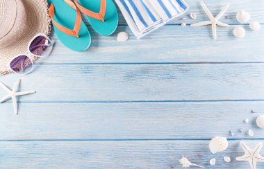 Yaz tatili, seyahat ve tatil konsepti. Güneş gözlüğü, denizyıldızı, plaj şapkası, terlik ve deniz kabuğu pastel mavi ahşap arka planda..