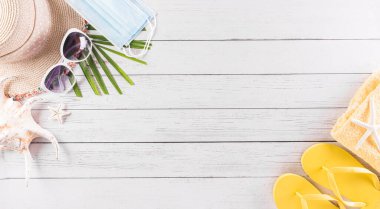 Yaz tatili, seyahat ve tatil konsepti. Güneş gözlüğü, denizyıldızı, plaj şapkası, deniz kabuğu ve tıbbi maske beyaz ahşap arka planda covid-19 'u korumak için..