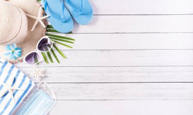 Yaz tatili, seyahat ve tatil konsepti. Güneş gözlüğü, denizyıldızı, plaj şapkası, deniz kabuğu ve tıbbi maske beyaz ahşap arka planda covid-19 'u korumak için..