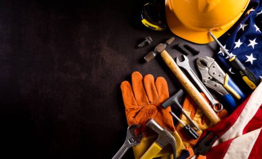 İşçi Bayramı konseptin kutlu olsun. Koyu taş zemin üzerinde farklı inşaat araçları bulunan Amerikan bayrağı.