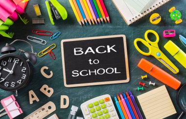 Eğitim ya da okula dönüş konsepti. Renkli okul malzemelerinin kitaplarla, renkli kalemlerle, hesap makinesiyle, kalem kesicilerle karatahta arka planıyla en iyi görünümü. Düz yatıyordu.