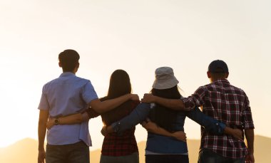 Bir grup mutlu arkadaş dağın önünde bir arada kalıp birlik ve takım çalışması göstererek gün batımının tadını çıkarıyorlar. Arkadaşlık mutluluğu eğlence ortaklık takım konsepti.