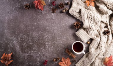 Sonbahar kompozisyonu. Bir fincan kahve, pamuk çiçekleri, sonbahar yaprakları ve koyu taştan arka planda kazak. Düz konum, kopyalama alanı olan üst görünüm.