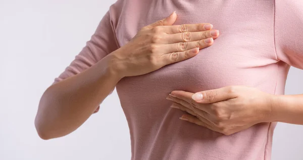 女性の手は 灰色の背景に乳がんの兆候のために彼女の胸の上に塊をチェックします 医療の概念 — ストック写真