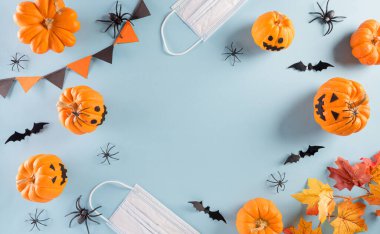 Cadılar Bayramı süslemeleri, pastel mavi arka planda balkabağı, kağıt yarasalar ve cerrahi maske. Covid-19 salgını sırasındaki Cadılar Bayramı kutlamalarının üst görüntüsü..