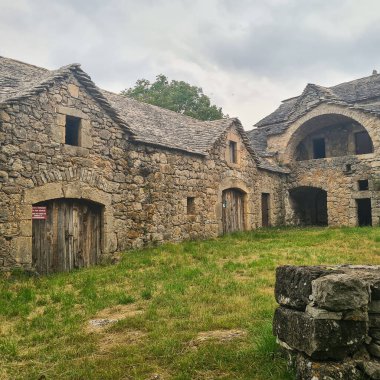 Fransa 'nın güneyindeki Lozere' de kırsal binalar, yıpranmış ahşap kapılar ve kireçtaşı mimarisi olan geleneksel taştan bir çiftlik evinin manzarası