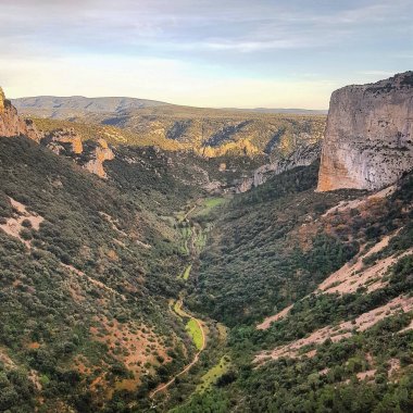 Dolambaçlı bir nehir, yeşil bitki örtüsü ve doğal bir dağ manzarasında güneşli tepeleri olan manzaralı bir vadi.