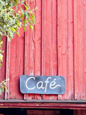 Kırmızı ahşap cephede klasik kafe tabelası. Kırsal kafe tabelası kırmızı ahşap duvarda. Kırsal kırmızı ahşap bir duvara, görünür ahşap desenli ve yıpranmış boyalı el yazısıyla yazılmış bir kafe tabelası asılmış. Açık kahve ya da kırsal restoran konsepti.