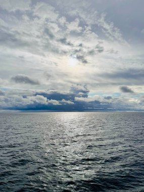 Açık denizde dramatik bulutlu bir gökyüzü ve su yüzeyine yansıyan güneş ışığı. Katmanlı bulutlar ve yayılmış güneş ışığıyla dramatik bir bulutun altında geniş deniz manzarası. Işık dokulu su yüzeyine hafifçe yansıyor..