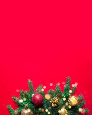 Alttaki kırmızı arkaplanda Noel için toplar ve konilerle süslenmiş köknar dalları var. Yanıp sönen Noel ışığı