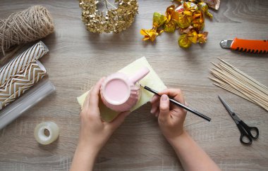 Kendine bir hediye yap. Bir buket tatlı, kupada bir kompozisyon. Adım adım talimatlar, ikinci adım: masanın üzerinde, bir adamın eli penoplex üzerinde pembe bir kupayı daire içine alıyor, kurumuş çiçeklerin yanında altın bir ortanca, makas, şeker, viski, musluk suyu.