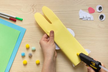 Paskalya tatlıları, çikolatayı paskalya tavşanı şeklinde sarmak. 14. adım: İnsan eli, Paskalya tavşanının kuyruğunu sıcak tutkalla yapıştırır. Hafif ahşap arka plan, renkli kağıt ve kalemlerin yanına.