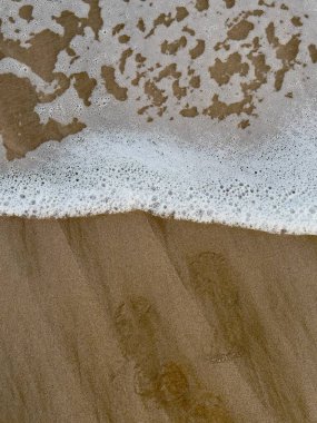 Islak kumun üzerindeki deniz köpüğünün minimalist görüntüsü yumuşak dokular ve barışçıl kıyı atmosferi yaratır. Sağlık ve tasarım için mükemmel.