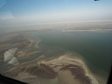 Küçük uçak penceresinden kumlu çöl manzarasının kanat ve gölgesini, açık gökyüzünün altındaki kurak arazinin hava perspektifini görüntüle.