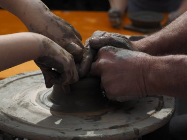 Seramik atölyesindeki bir çömlek çarkında ıslak kil şekillendiren eller, geleneksel el işi tekniği ile el yapımı çömlek yapan bir zanaatkar..