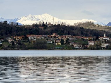 Kuzey İtalya 'daki Corgeno Gölü' nde doğal göl manzarası. Sazlıklar ve ağaçlar parçalı bulutlu bir gökyüzünün altında durgun suyu çerçeveliyor. Huzurlu manzara kırsal atmosfer, biyolojik çeşitlilik ve açık hava sükunetini yakalıyor.
