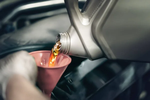 Trabajador vierte nuevo aceite de motor sintético de la lata en el motor del coche en servicio —  Fotos de Stock