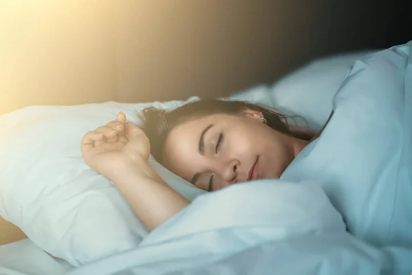 Beautiful young girl or woman sleeping sweetly in bed in early morning in rays of dawn, close up portrait — Stock Photo, Image