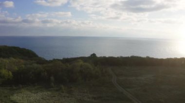 Mavi deniz kıyısının hava panoramik görüntüsü, güneş ışığında kayalıklardaki yeşil ormandan sonra açılıyor. Karadeniz, inanılmaz vahşi doğa.