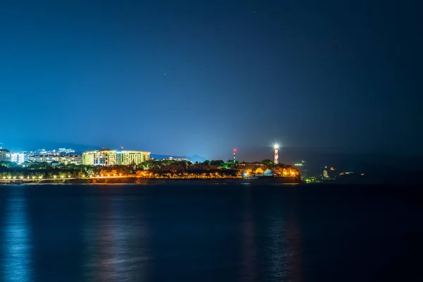 Sea night landscape with cape, illuminated buildings and lighthouse