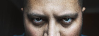 Kızgın ya da yorgun, torbalı ya da ürkütücü gözlerinin altında siyah halkalar olan kötü görünüşlü erkek portresi. Korkunç iblis ya da kötü negatif insan kameraya bakar.