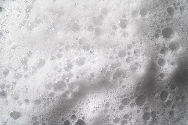 White foam with bubbles texture, soap, detergent or shampoo or cleanser surface, macro shot. Body care concept