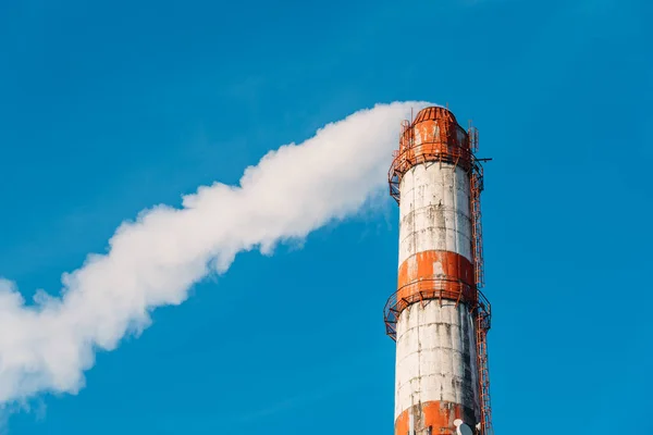 Industrial smoke stack of metallurgical factory with white vapor on blue sky background