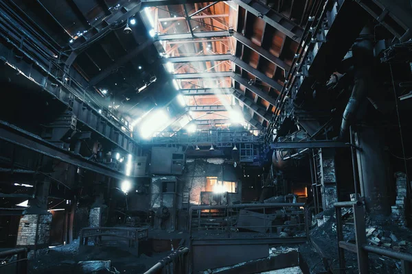 Hangar gelap besar tua berkarat meninggalkan industri pabrik metalurgi di bawah sinar matahari yang bersinar melalui lubang di atap usang — Stok Foto