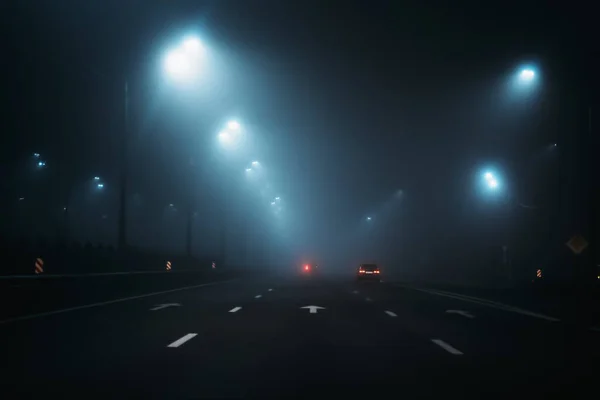 Dark road with city illumination in misty and foggy night
