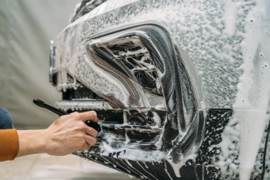 Oto yıkamada detaylı araç temizliği İşçi tamponu köpük ve fırçayla temizliyor