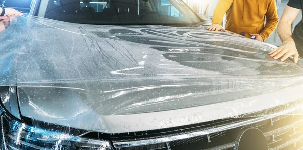 Los trabajadores envuelven película de protección de pintura húmeda o revestimiento de protección contra la grava en la capucha del coche nuevo. Detallado del coche — Foto de Stock