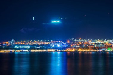 Gelendzhik tatil beldesi kıyı şeridi üzerindeki dağlardaki Rusça dilinde parlayan GELENDZHIK sözcüğü gece deniz suyu yüzeyine yansıyan set veya gezinti güvertesi ve aydınlatılmış binalarla yankılanıyor