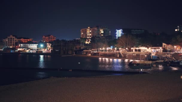 Gelendzhik havet resort strand kust på natten med upplysta moderna byggnader på bakgrunden återspeglas i havsytan — Stockvideo