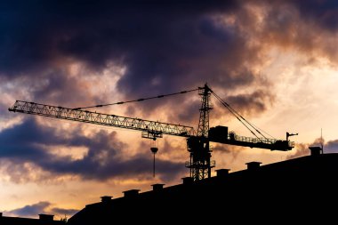 Günbatımında gökyüzü arka planında endüstriyel vinç ve bina silueti