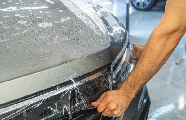 Película de protección del coche o proceso de PPF de envolver e instalar en la capucha del coche por las manos del trabajador detailer, primer plano —  Fotos de Stock