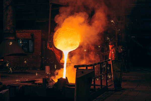 Metallurgical plant, hot liquid metal pouring into special mold in foundry with worker